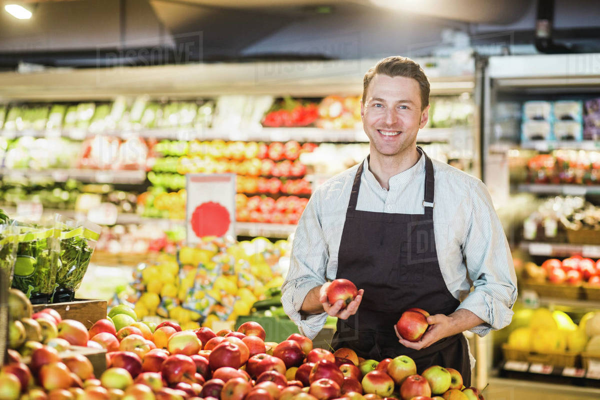 Portrait of smiling mature owner standing at apple stall in grocery