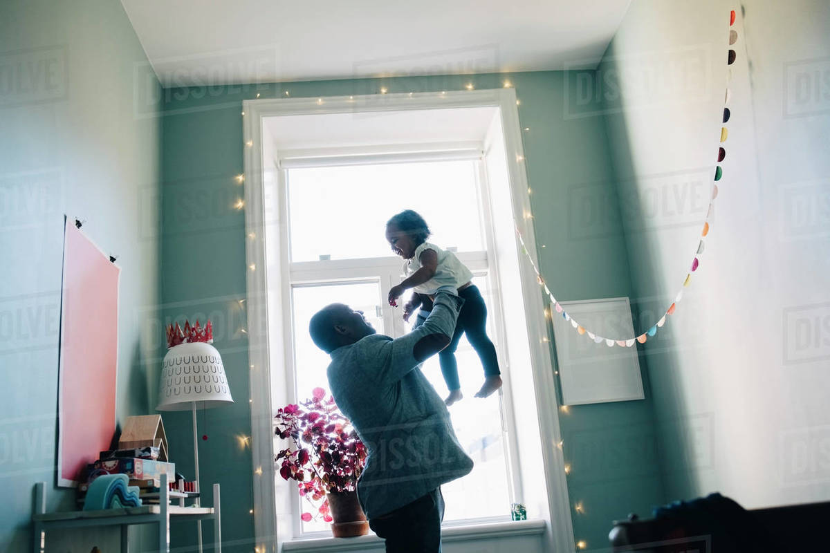 Side view of happy father holding daughter while standing by window at home Royalty-free stock photo