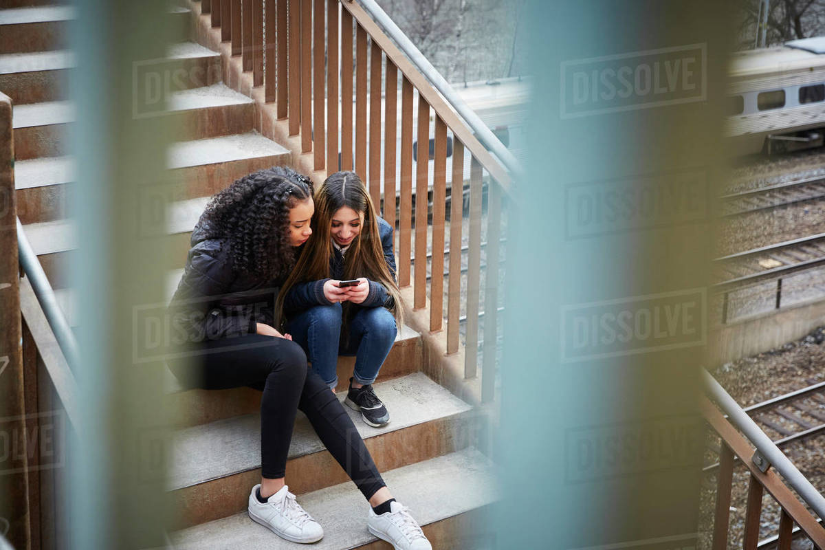 Teenage girl showing mobile phone to female friend while sitting on steps Royalty-free stock photo