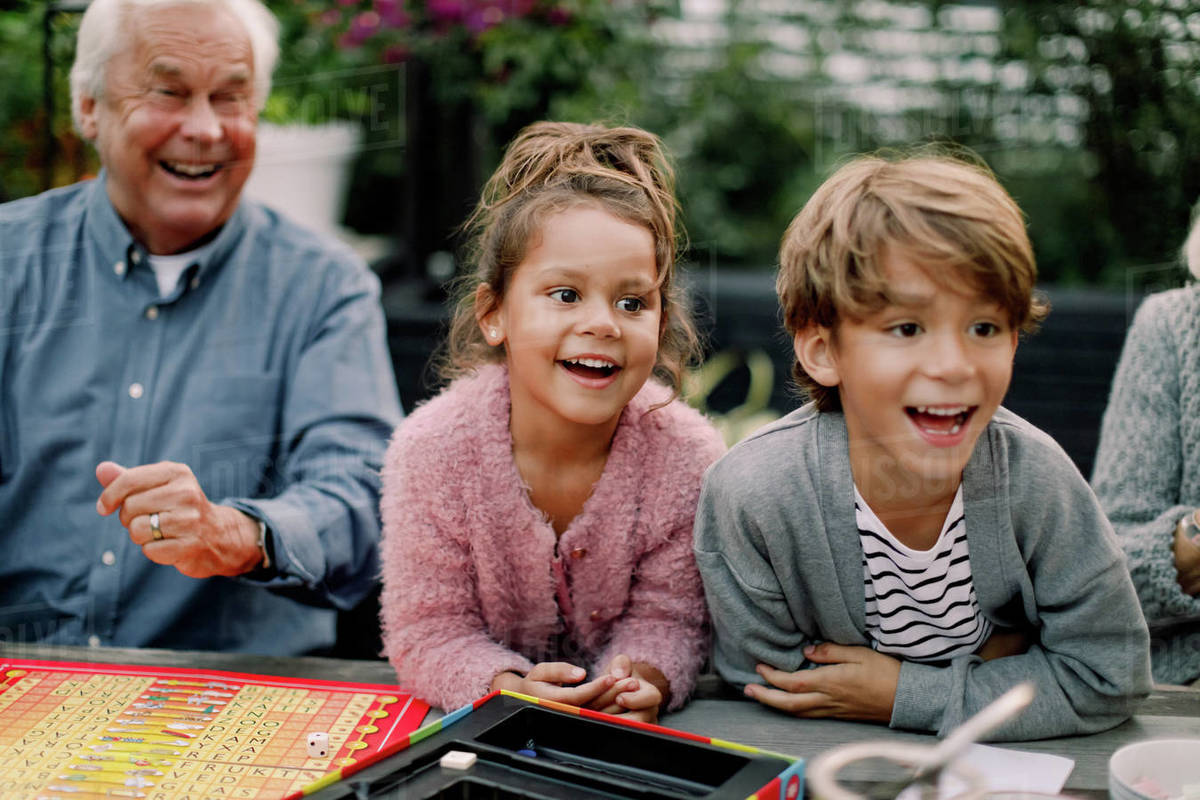 Smiling grandchildren playing board game with grandparents on table in