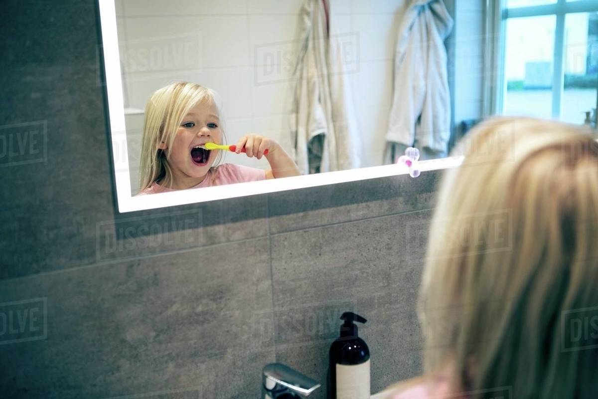 Reflection of girl brushing teeth seen on bathroom mirror Stock Photo