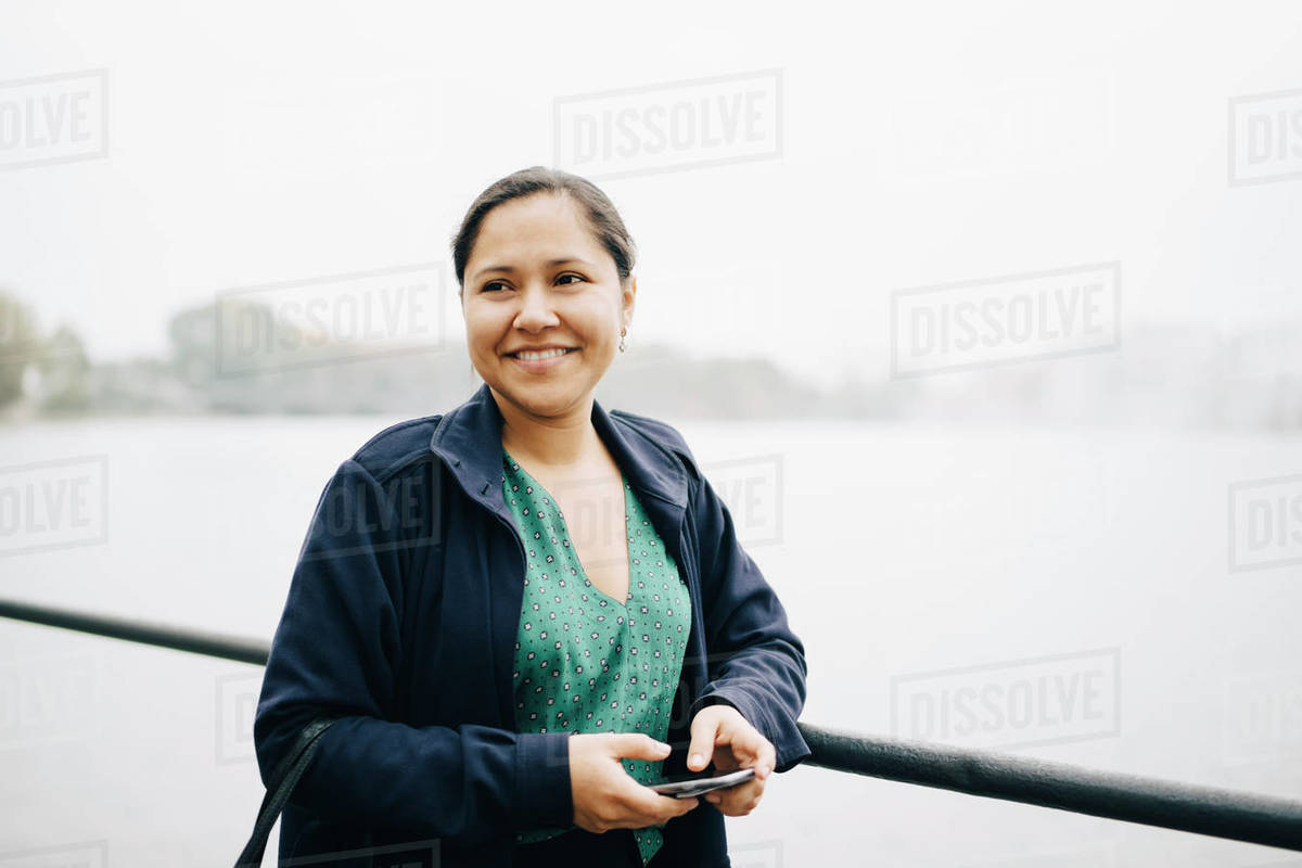 Smiling female entrepreneur with phone standing against sea in city Royalty-free stock photo