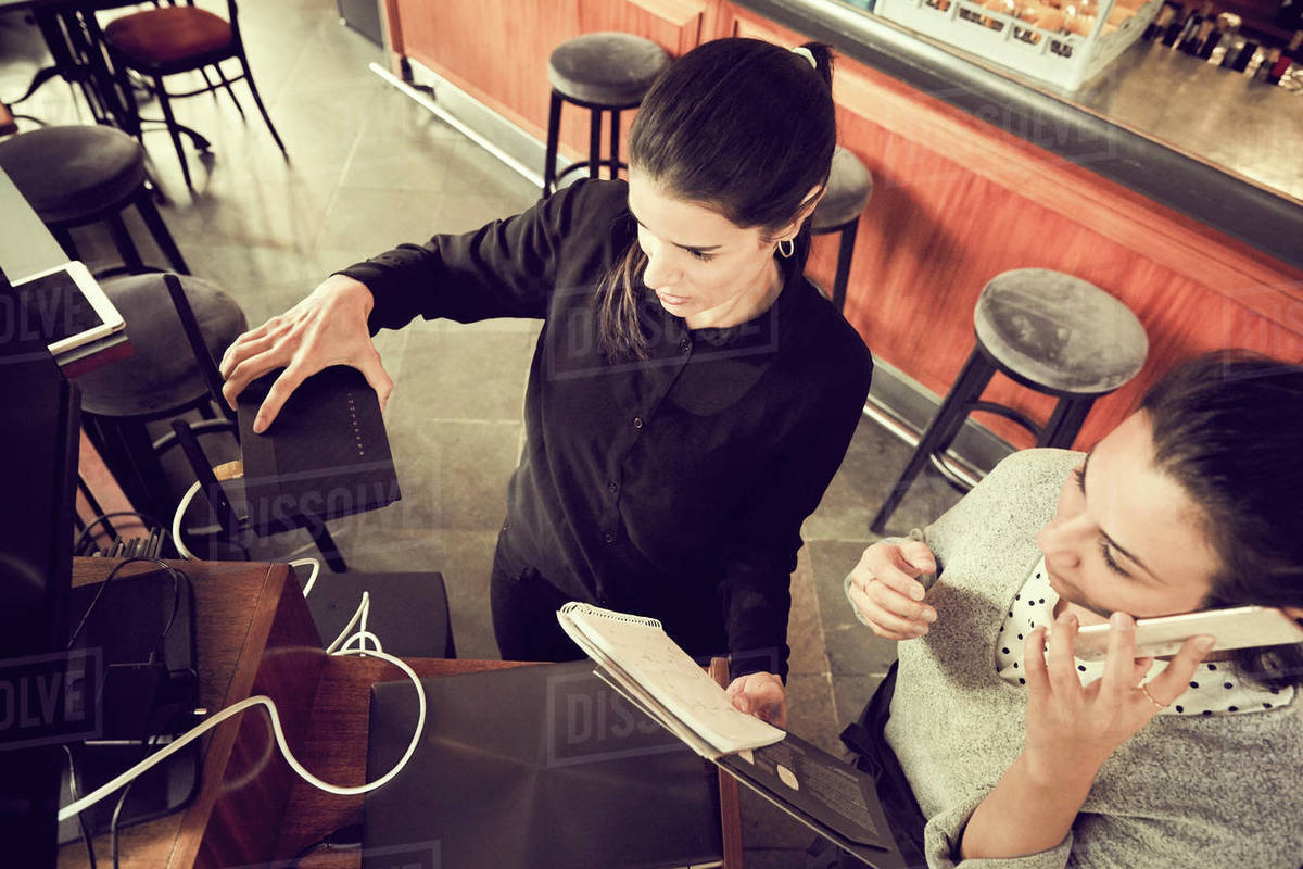 High angle view of owner holding modem while colleague talking through smart phone in cafe Royalty-free stock photo