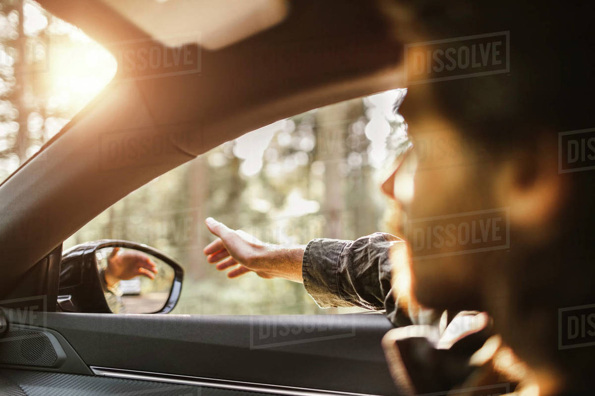 Young man with hand outside car window looking away during road trip