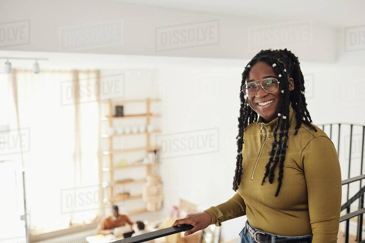 Portrait of smiling female computer programmer standing by railing at ...