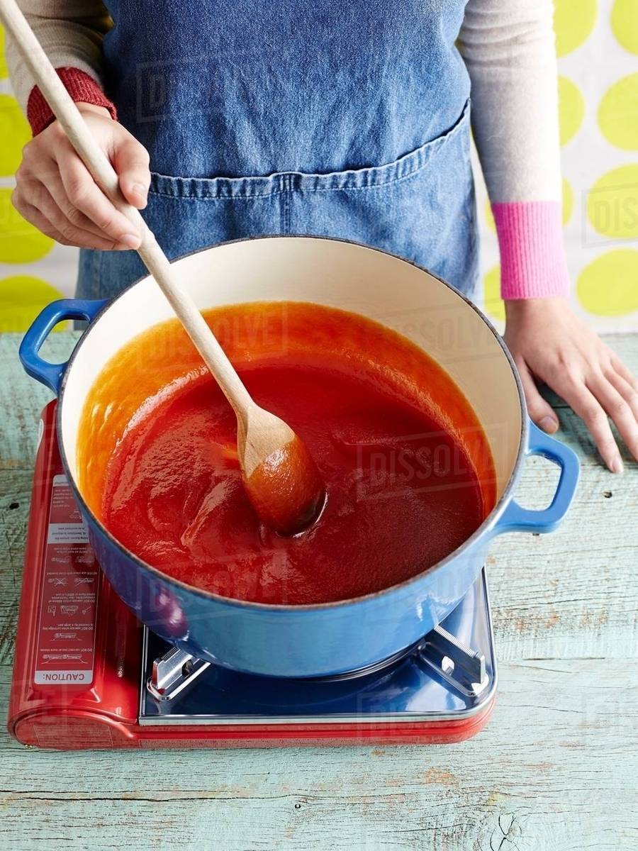 Woman preparing tomato ketchup recipe step 3, stirring pureed tomatoes