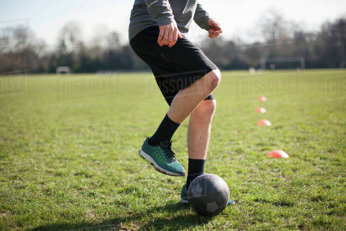 Waist down of young man practicing soccer on playing field Stock