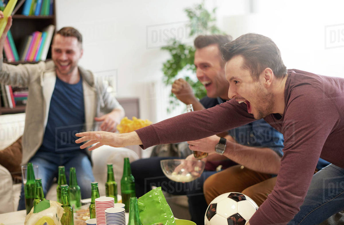 Group of men watching sporting event on television holding football