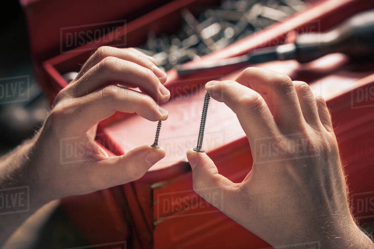 Fingers holding different sized screws Stock Photo Dissolve