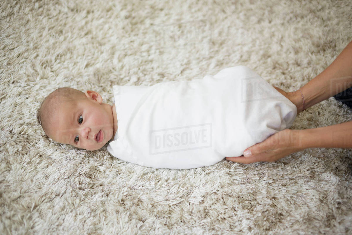 Swaddling Step 6. Mother finishing tucking in baby boy with blanket