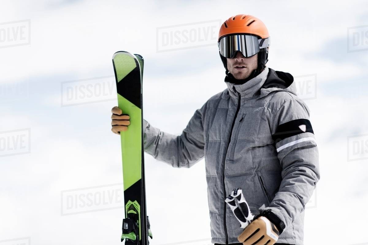 Man wearing helmet and ski goggles holding skis, portrait Stock Photo