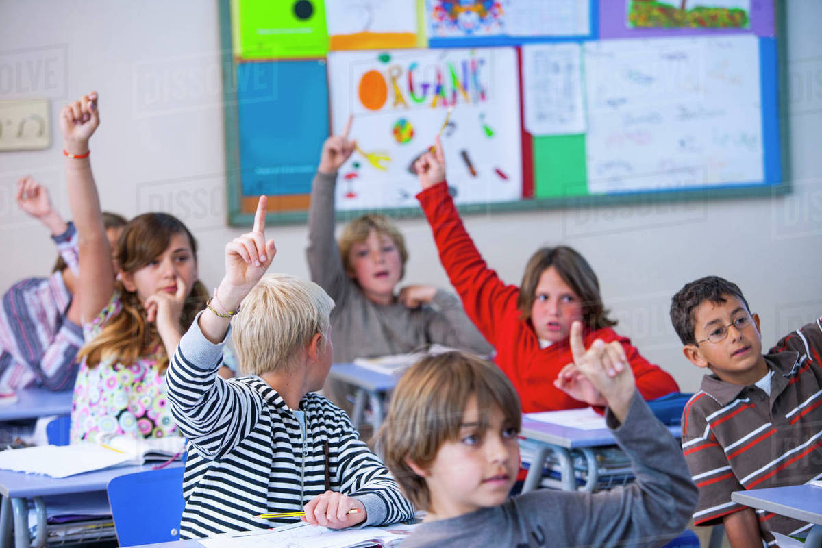Students in classroom, sitting at desks, with arms raised - Royalty ...