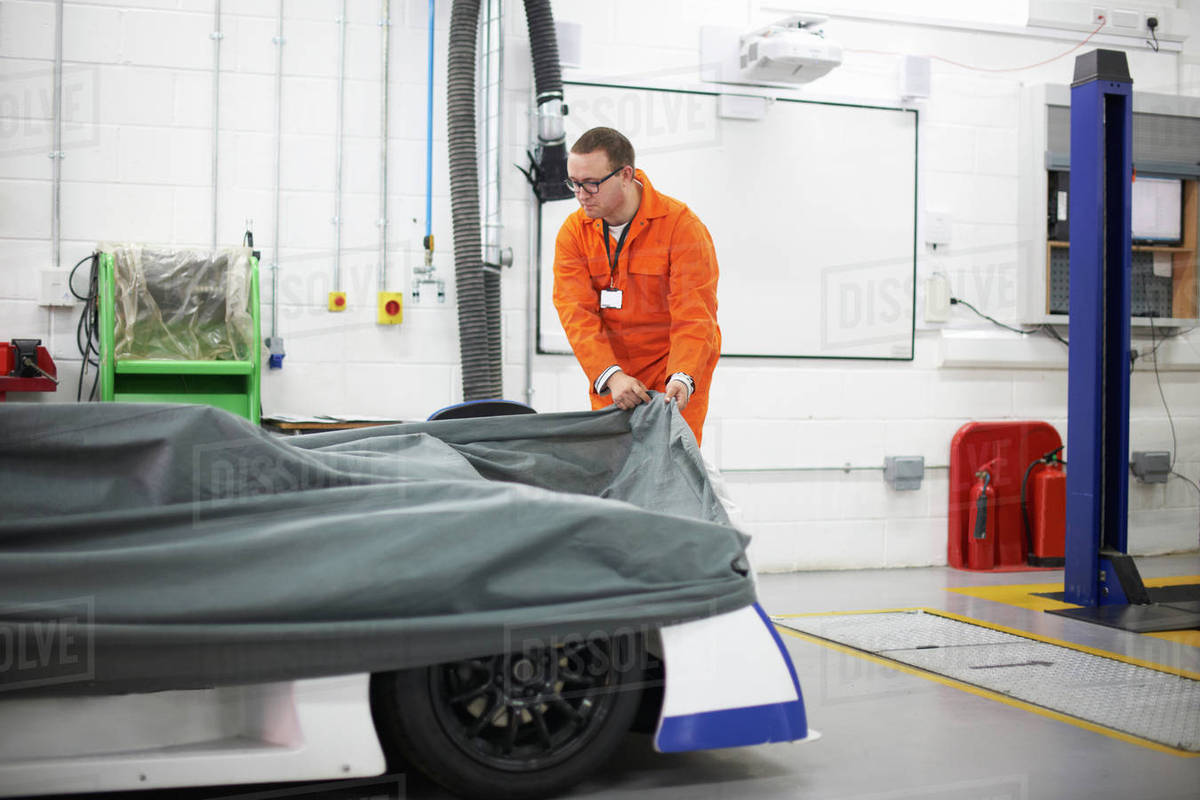 College mechanic student removing racing car cover in repair garage