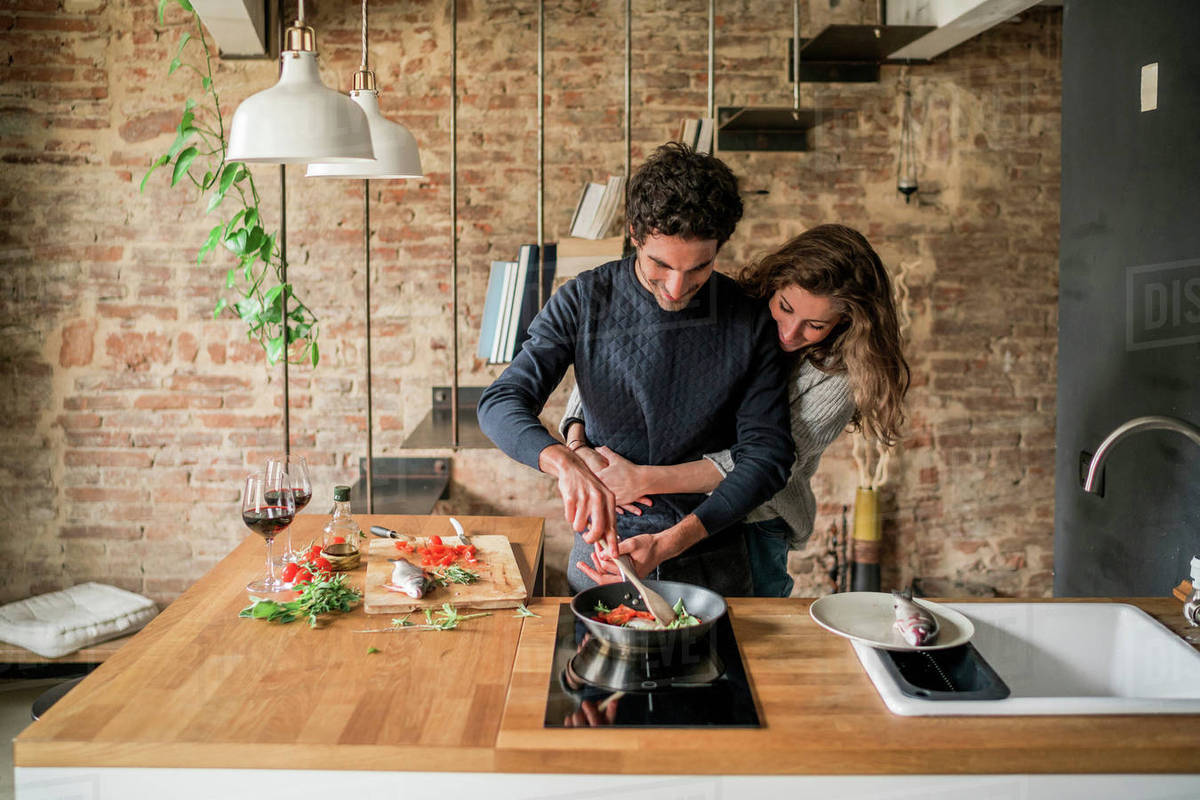Young couple cooking fish cuisine at kitchen counter hob Stock Photo
