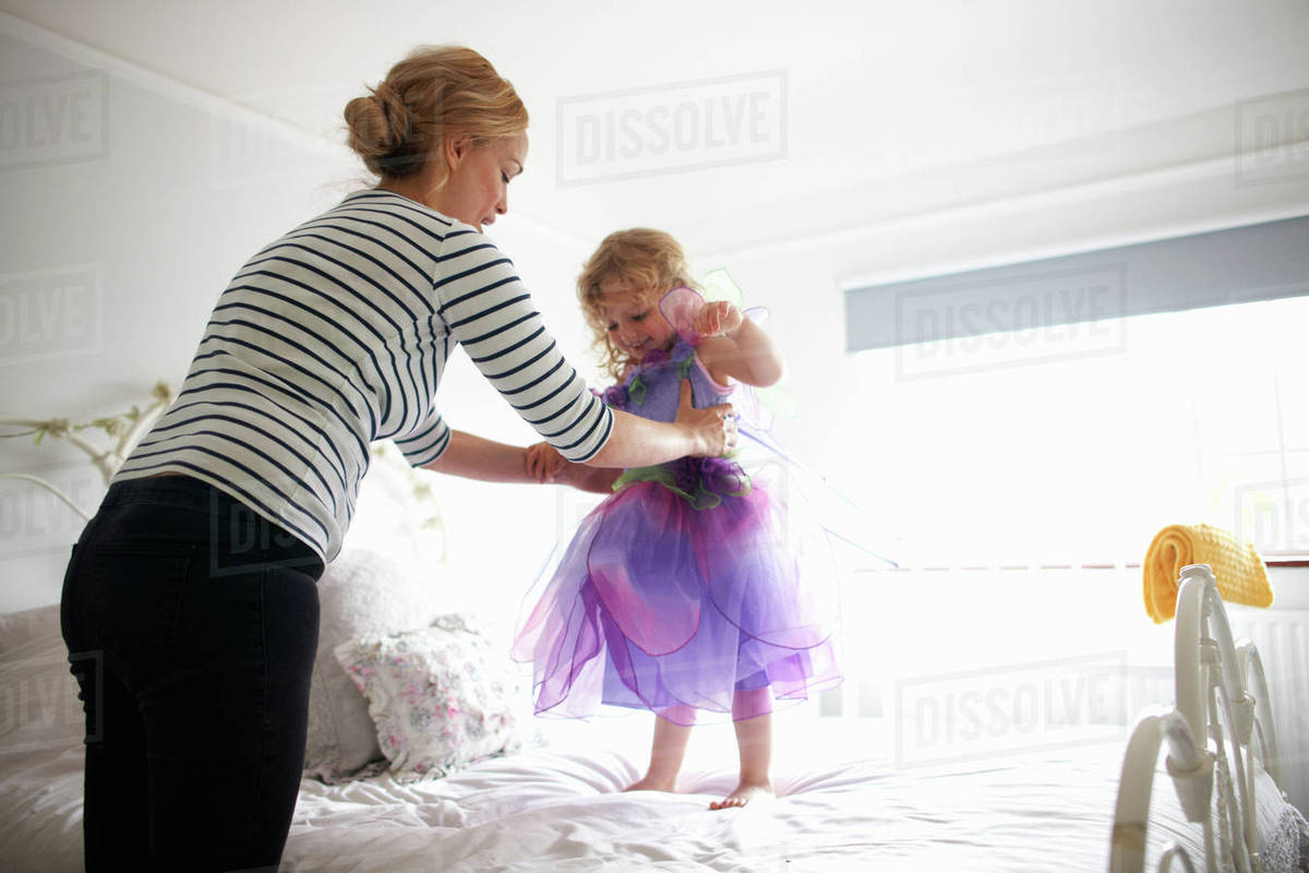 Young girl dressed in fairy costume, standing on bed, mother lifting her Royalty-free stock photo