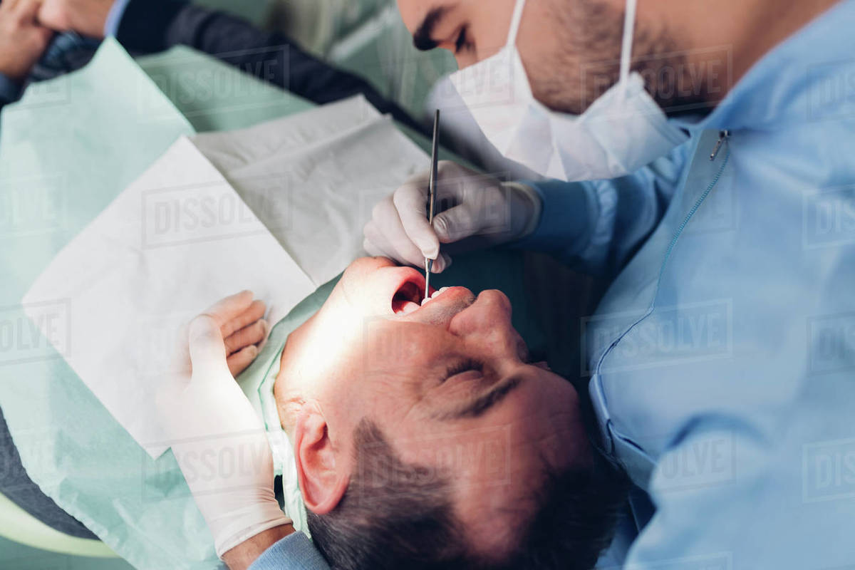 Dentist looking into male patient's mouth, elevated view Stock Photo Dissolve