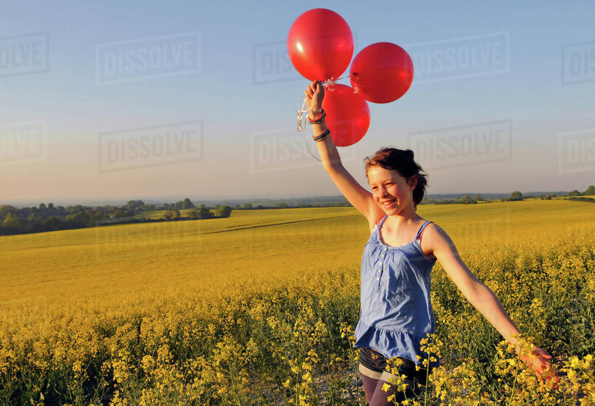 Girl with red balloons on rapeseed field, Eastbourne, East Sussex