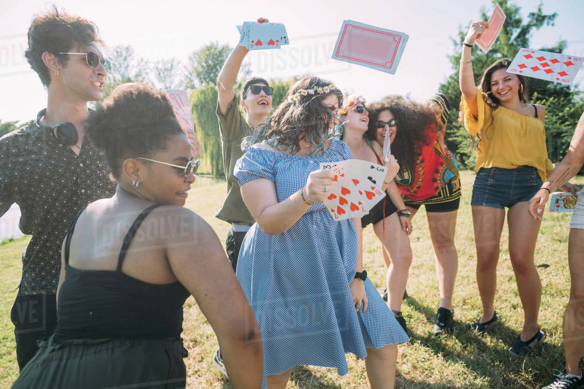 Group of friends dancing, throwing playing cards into air in park