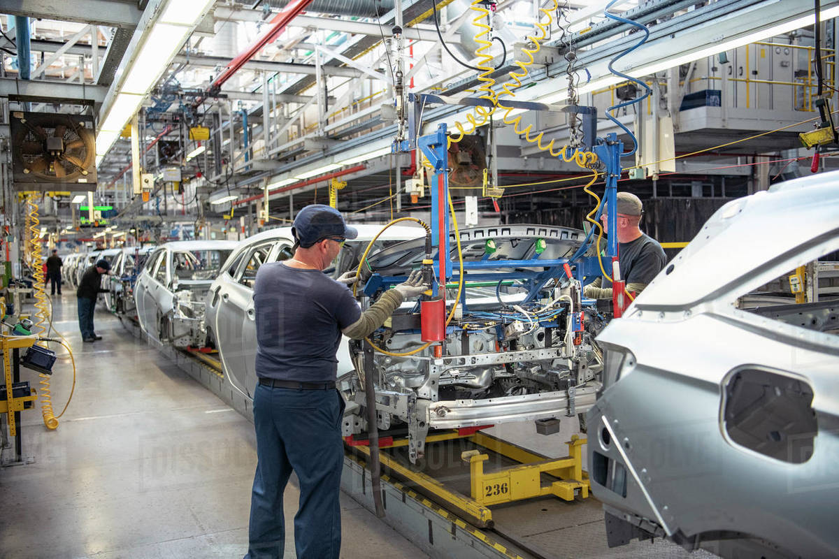 Car workers fitting to cars on production line in car factory