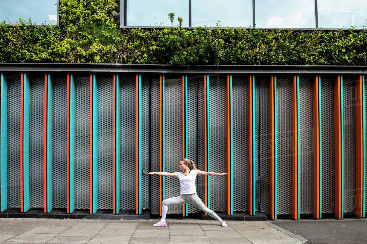 Young woman practicing yoga pose on city sidewalk, arms and legs outstretched Royalty-free stock photo