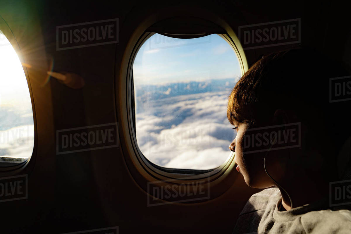 Teenage boy looking out through airplane window at clouds on airplane journey Royalty-free stock photo