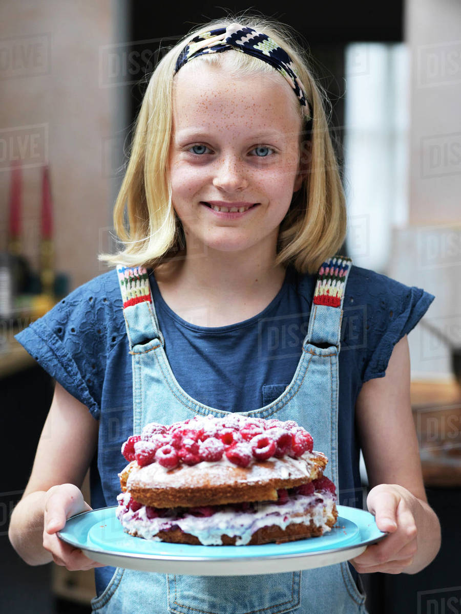 Girl baking a cake, holding homemade cake with raspberries on top in kitchen, portrait Royalty-free stock photo