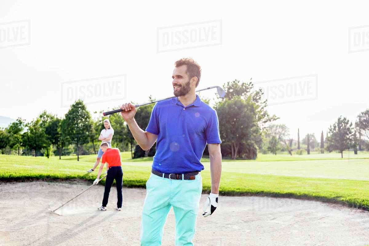 Man carrying golf club on golf course, friends playing golf in