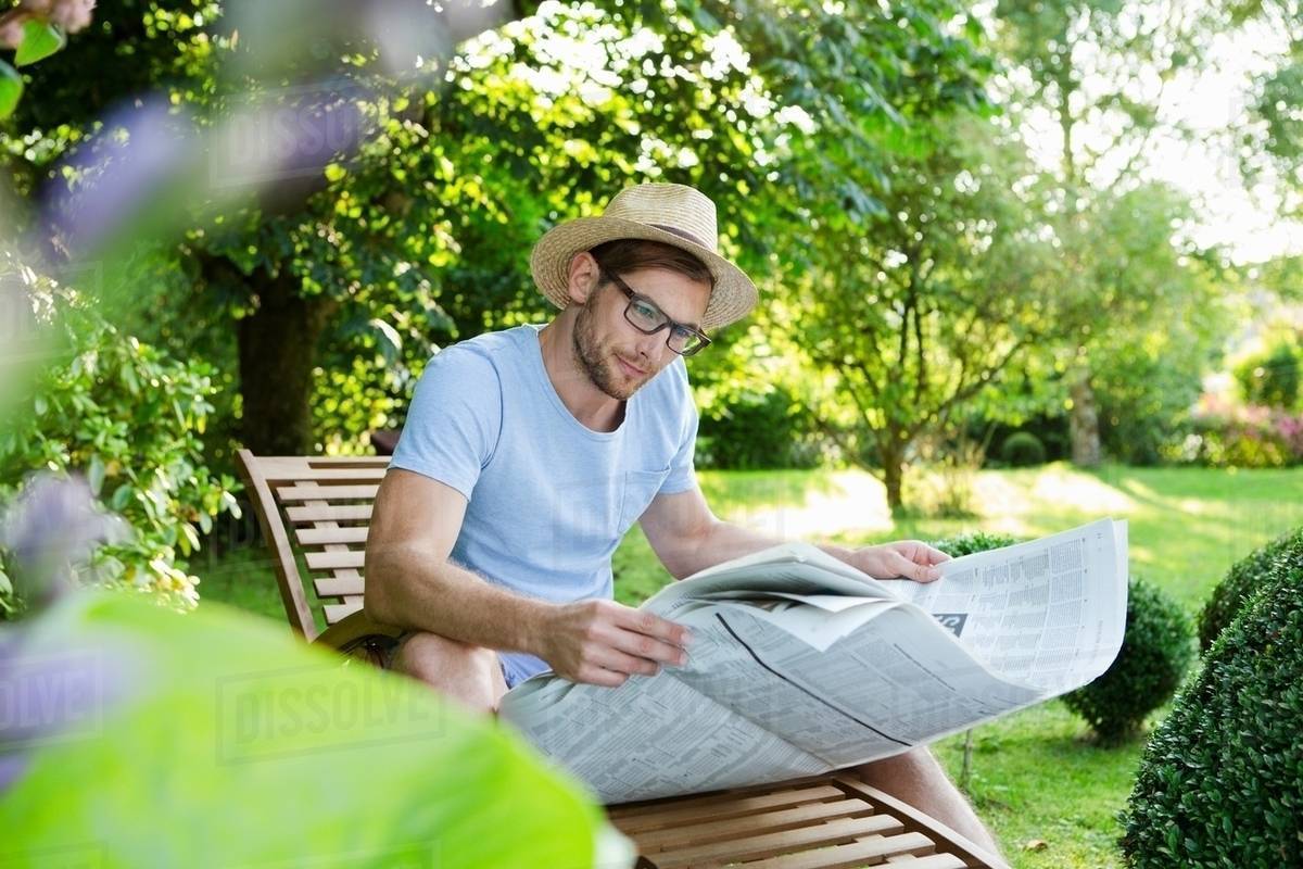 Mid adult man reading newspaper in garden Stock Photo Dissolve