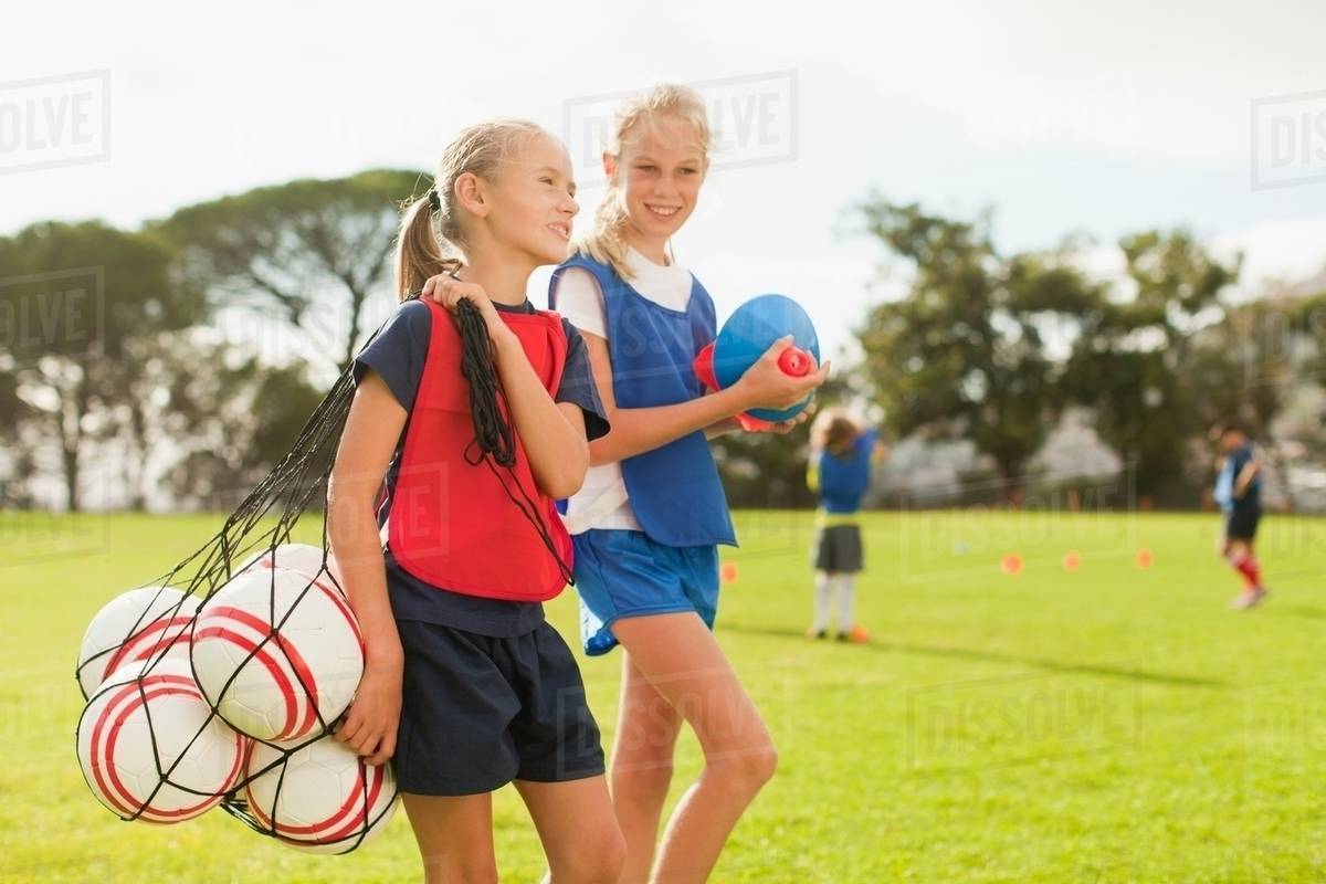 Girl carrying soccer balls on pitch Stock Photo Dissolve