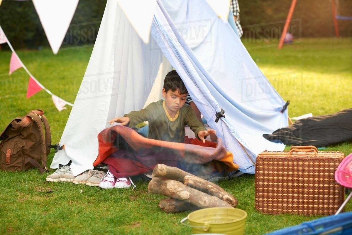 Boy shaking blanket from homemade tent in garden Stock Photo Dissolve