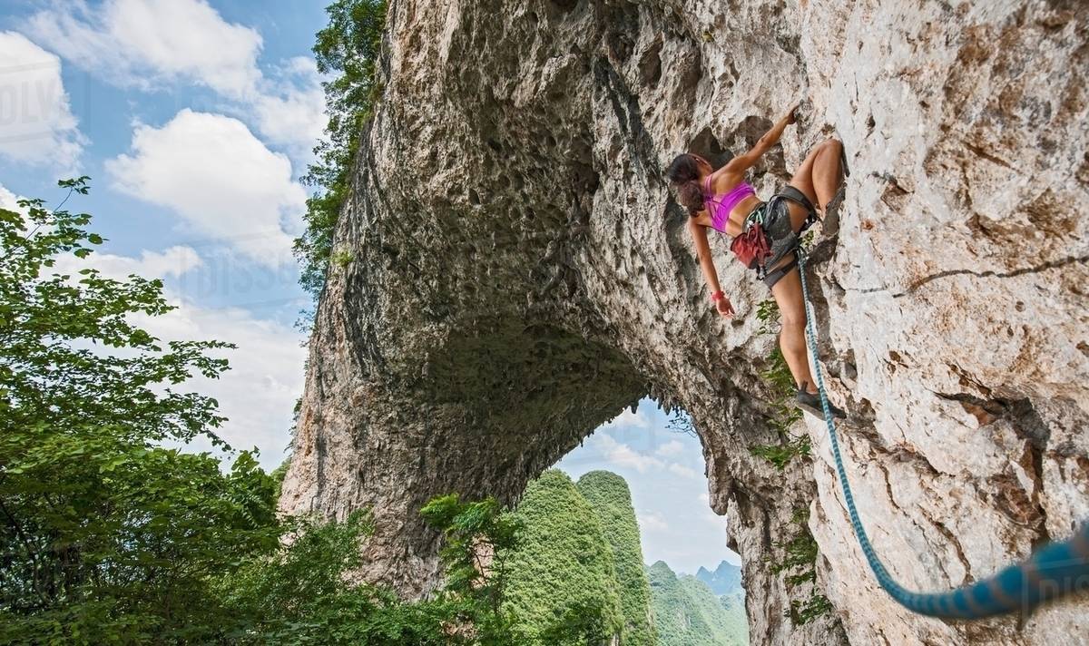 Female climber climbing on Moon Hill limestone arch in Yangshuo, Guangxi Zhuang, China Stock