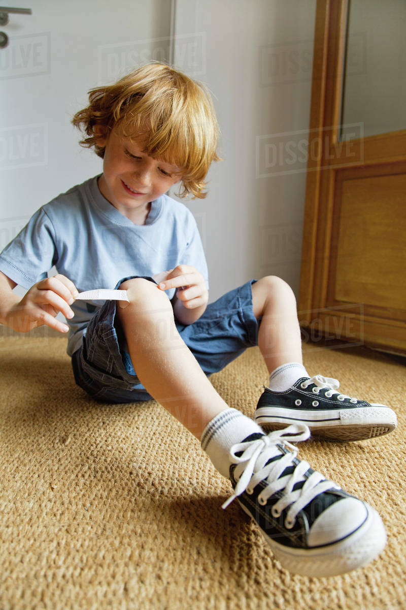 Boy removing adhesive bandage from knee Stock Photo Dissolve