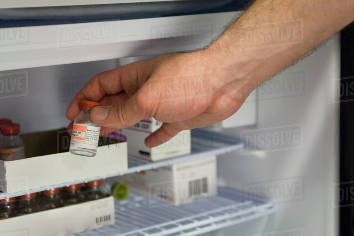 Healthcare professional removing vial of medication from refrigerator