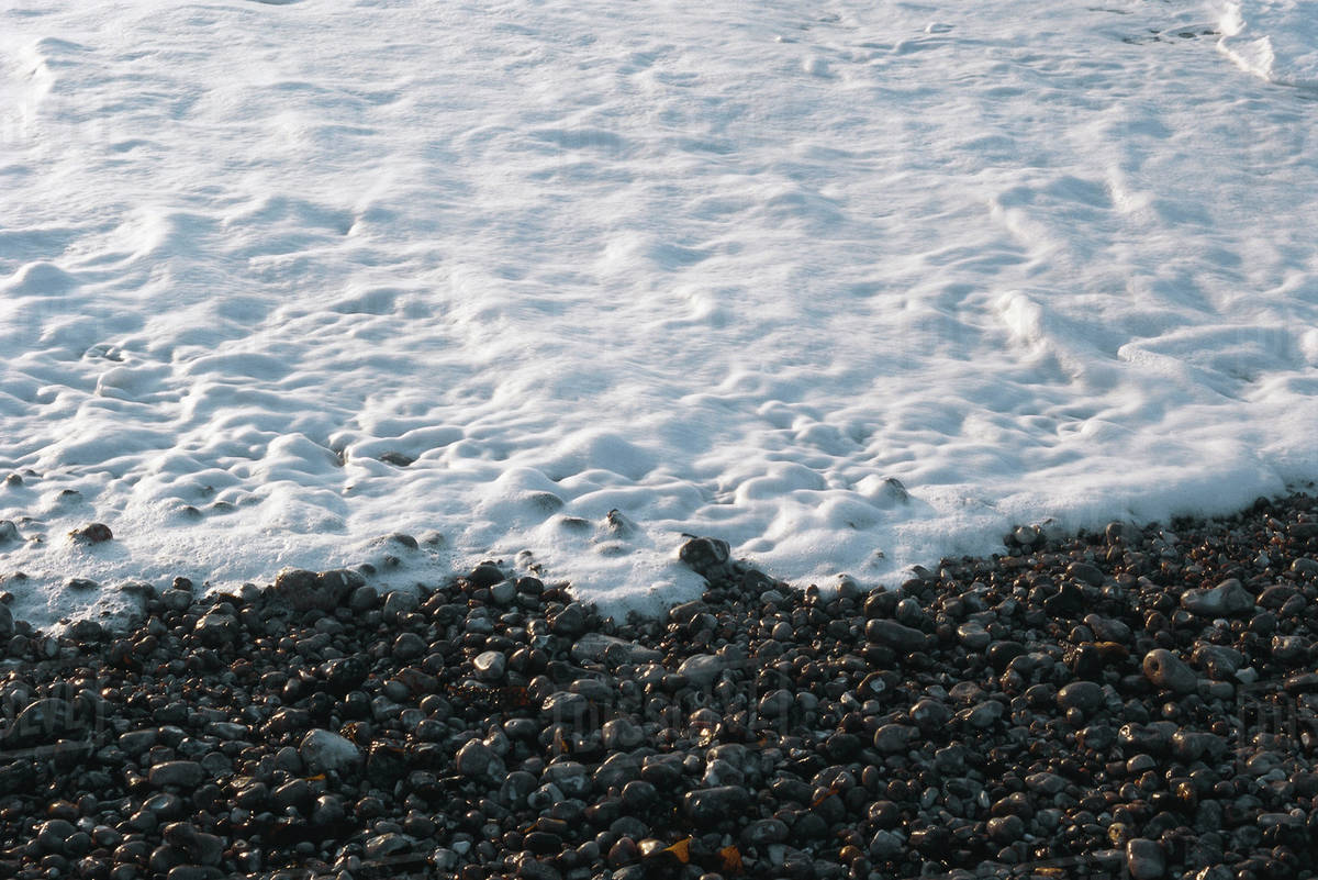 Foamy surf on pebble beach Stock Photo Dissolve
