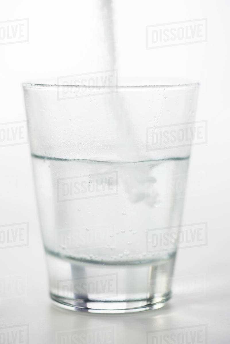 Pouring powdered medicine into glass of water Stock Photo Dissolve