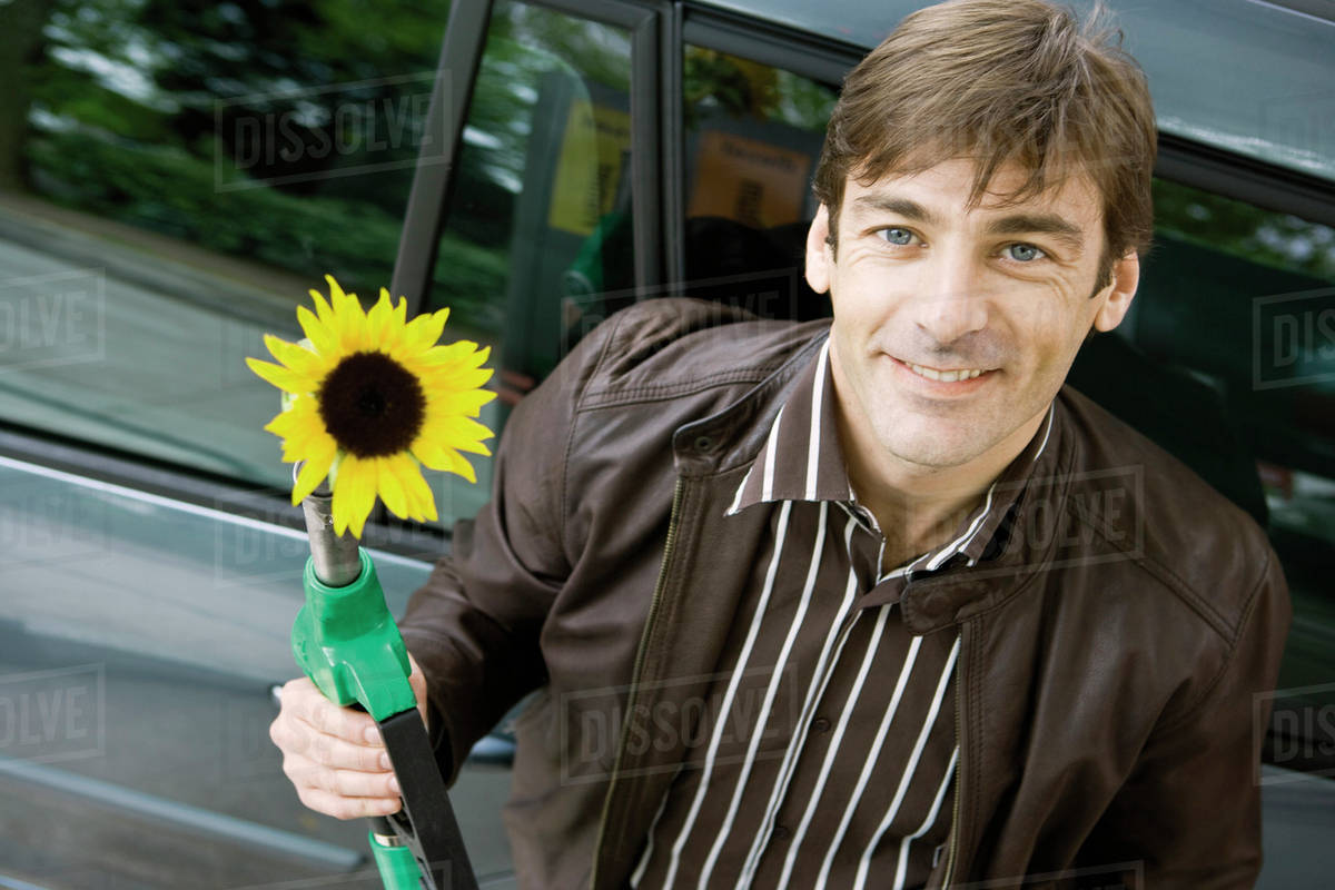 Man at gas station holding gas nozzle with sunflower emerging from end