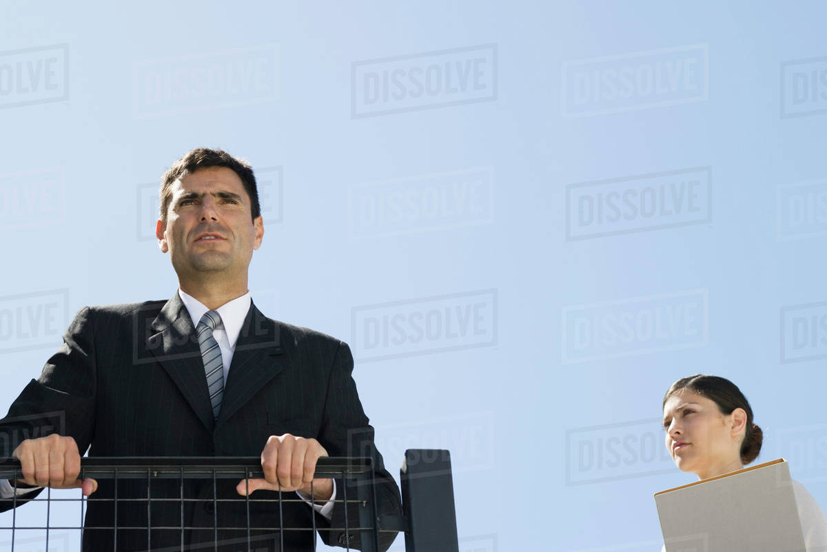 Businessman gripping railing and looking in the distance, assistant ...