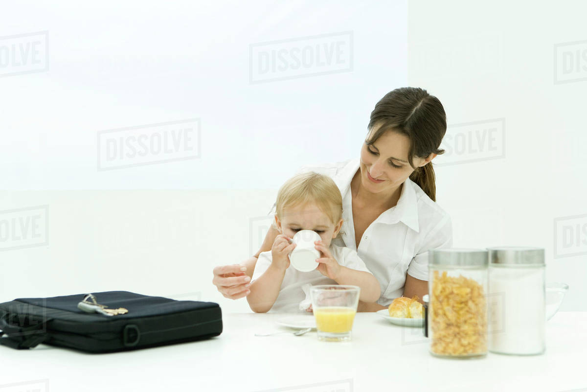 Professional woman sitting at breakfast table with toddler, briefcase nearby Stock Photo
