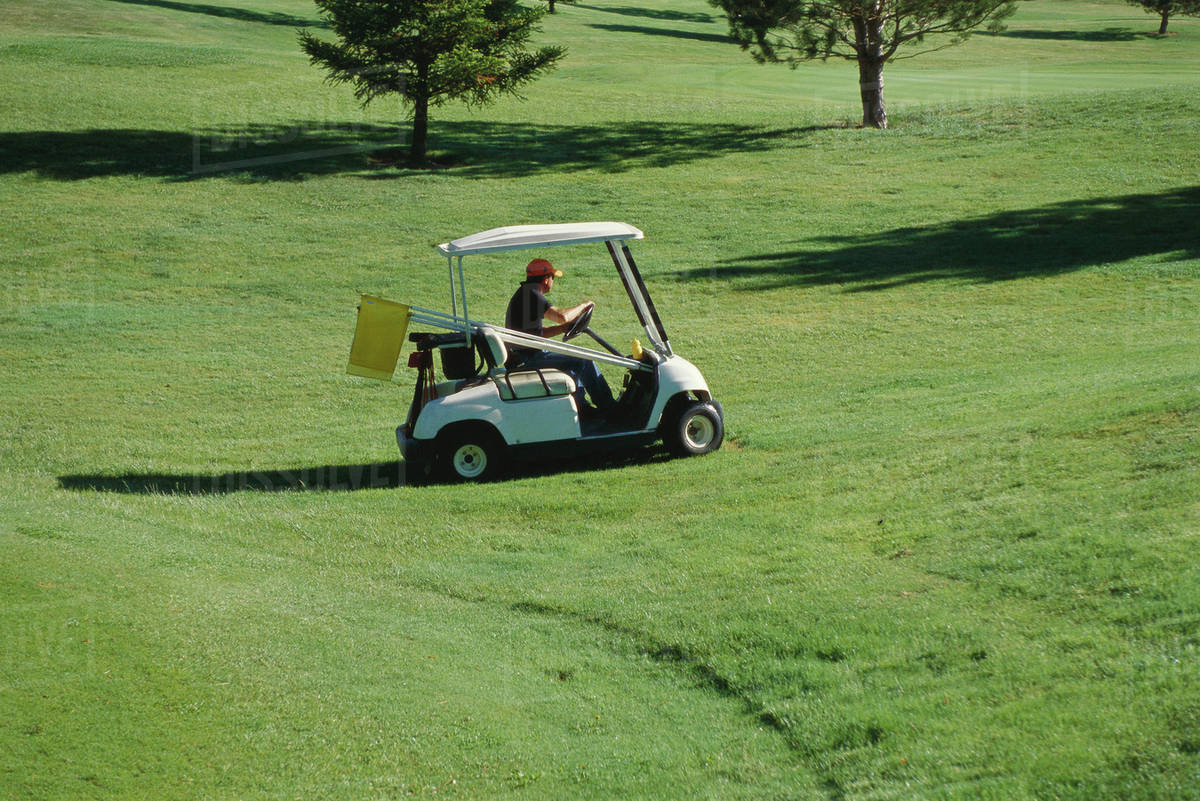 Groundskeeper driving golf cart across course Stock Photo Dissolve