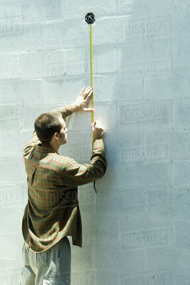 Man using measuring tape on cinder block wall Stock Photo Dissolve