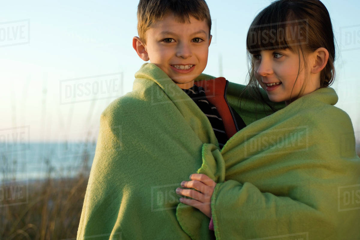 Children wrapped together in blanket outdoors, portrait Stock Photo Dissolve
