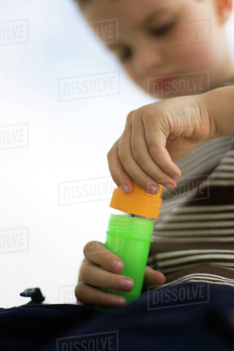 Little boy opening bottle of bubbles, low angle view Stock Photo Dissolve