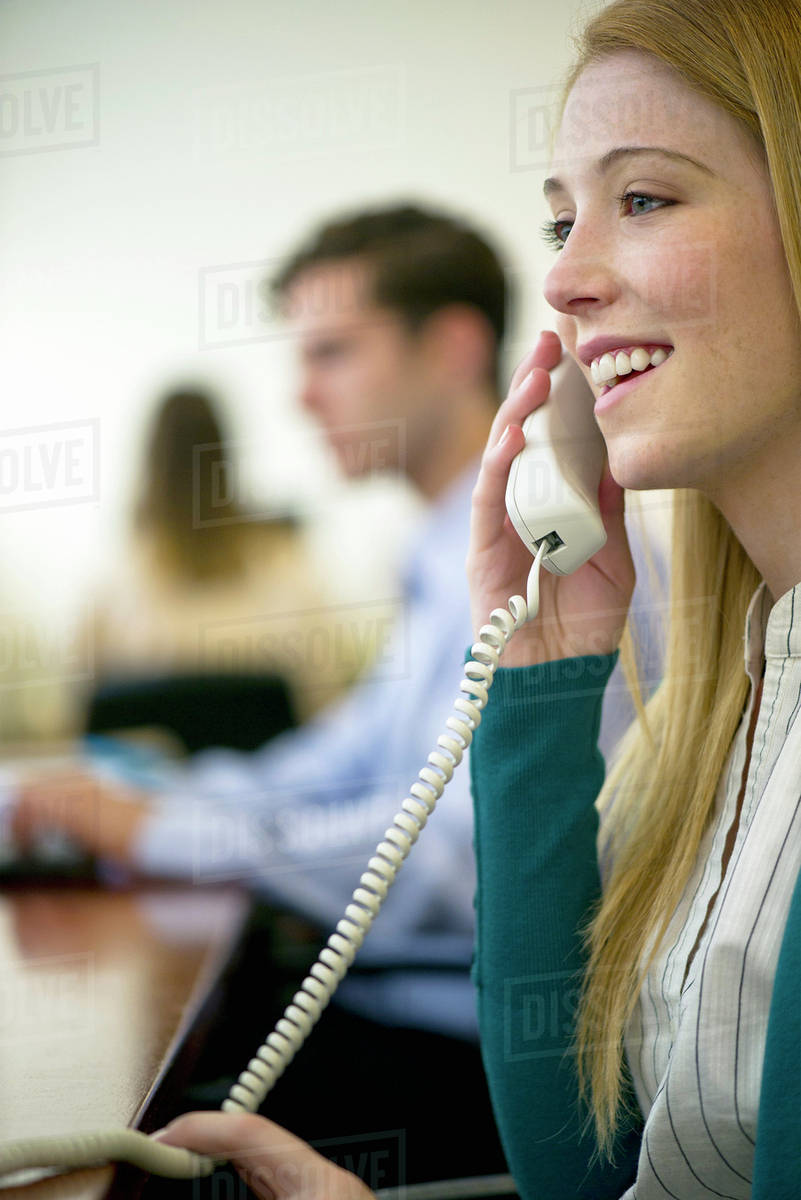 Woman using landline phone in office Stock Photo Dissolve