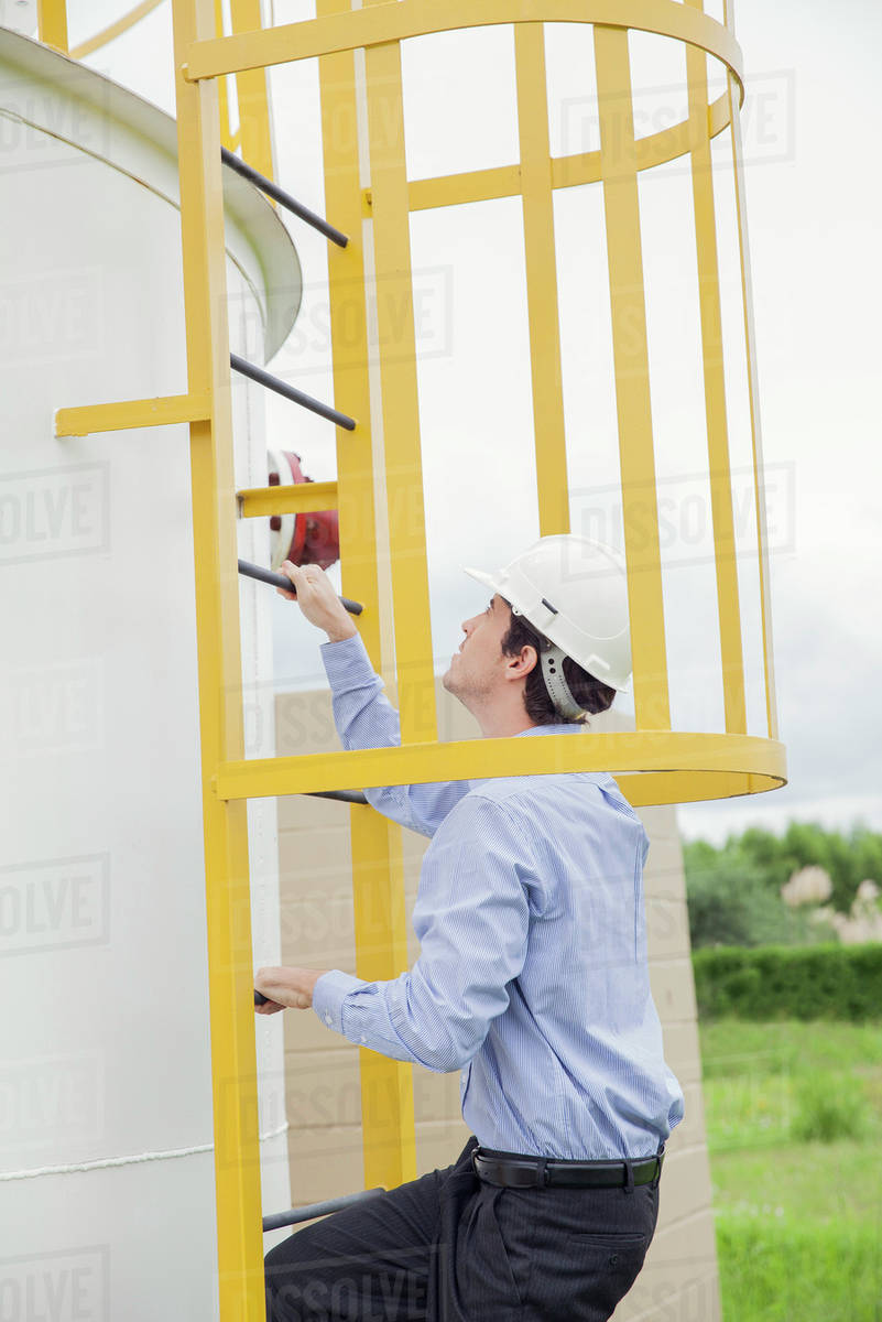 Engineer climbing storage tank ladder at industrial site Stock Photo