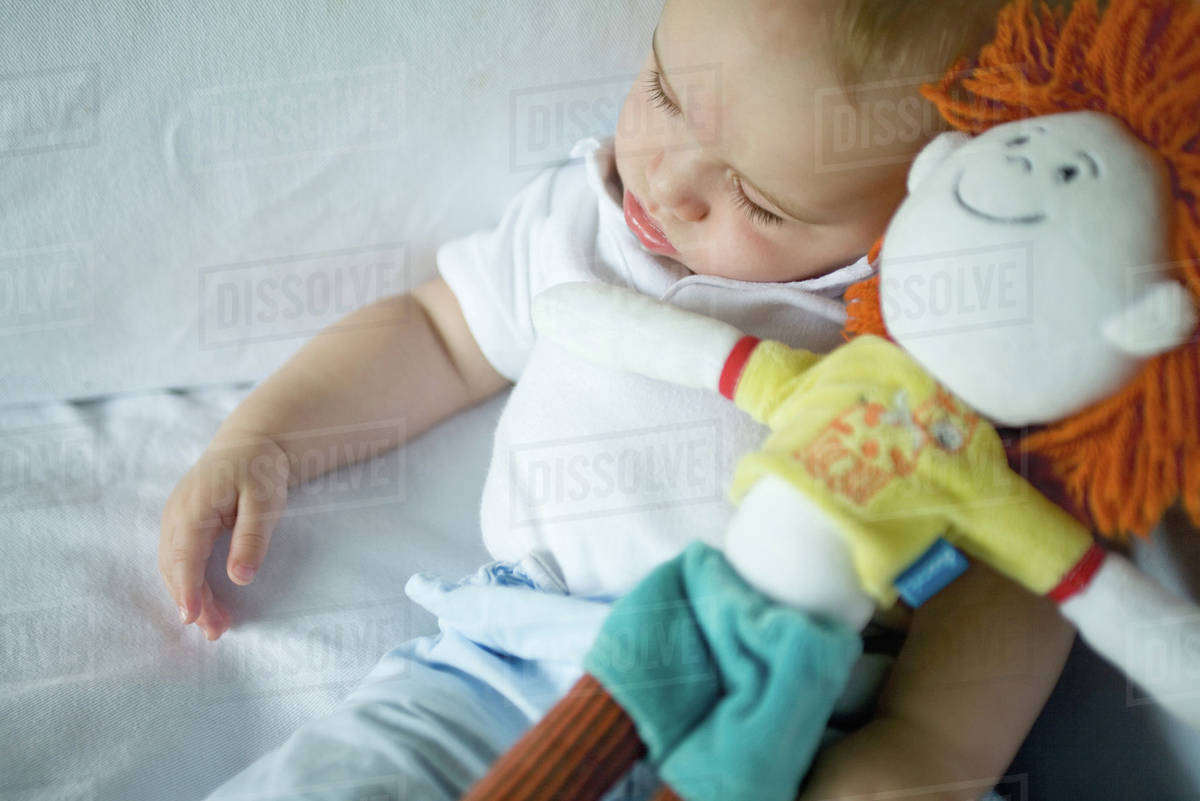 Baby sleeping, holding doll Stock Photo Dissolve