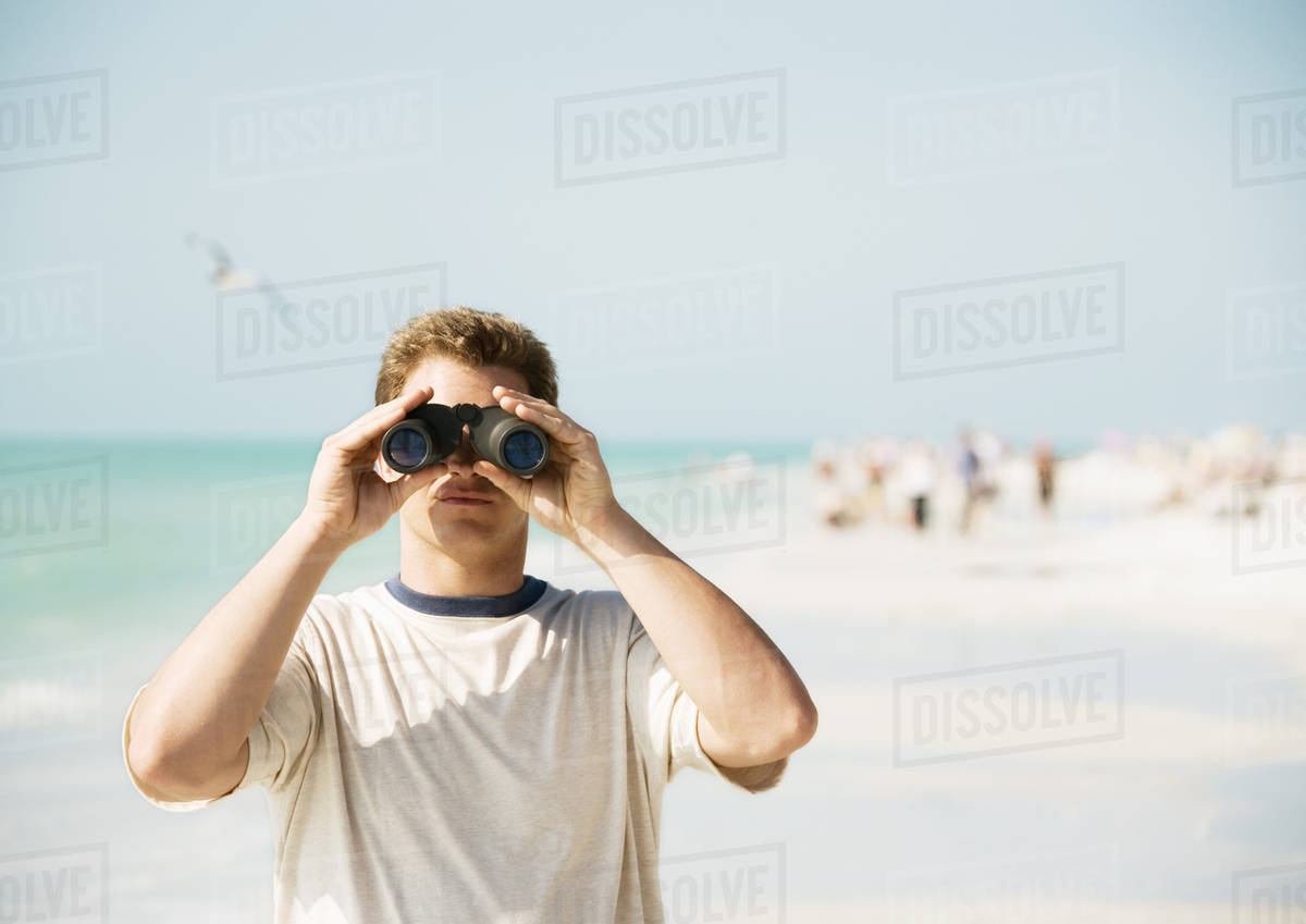 Man looking through binoculars on beach, facing camera Stock Photo