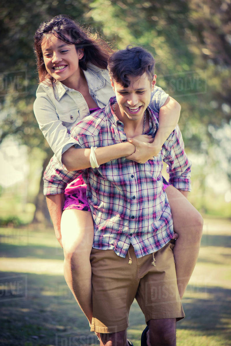 Man giving girlfriend piggyback ride in park Stock Photo Dissolve
