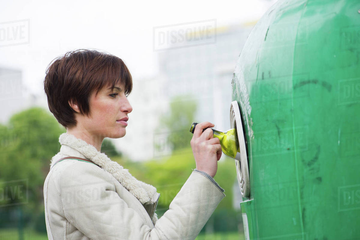 Woman putting wine bottle into recycling bin Stock Photo Dissolve