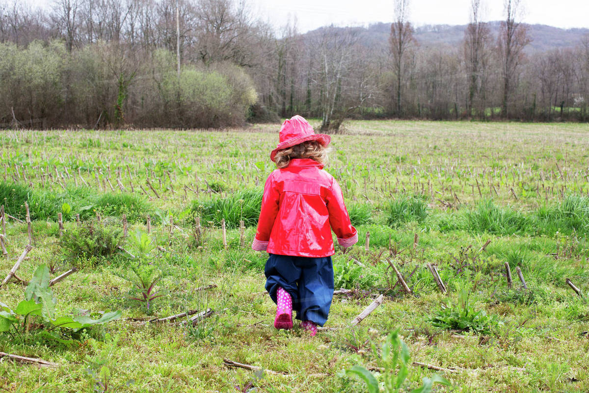 Little girl wearing rain gear playing in field Stock Photo Dissolve