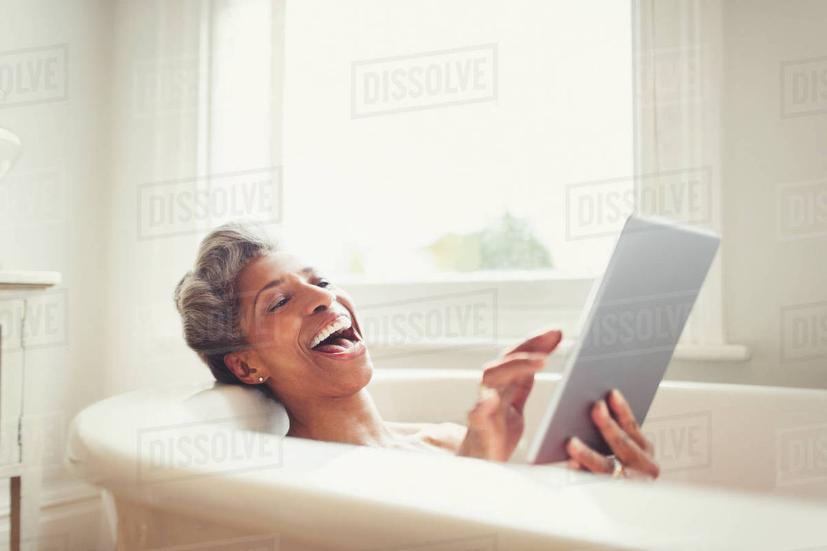 Laughing mature woman using digital tablet in bathtub Royalty-free stock photo